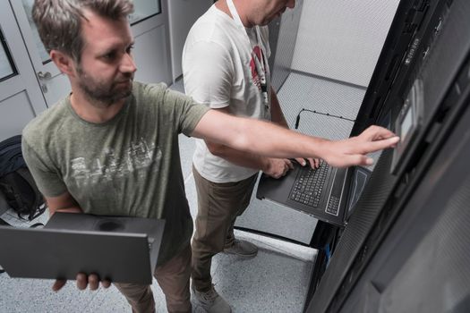 A couple of server engineers cooperate in high tech data centers. Technicians team updating hardware inspecting system performance in super computer server room or cryptocurrency mining farm.