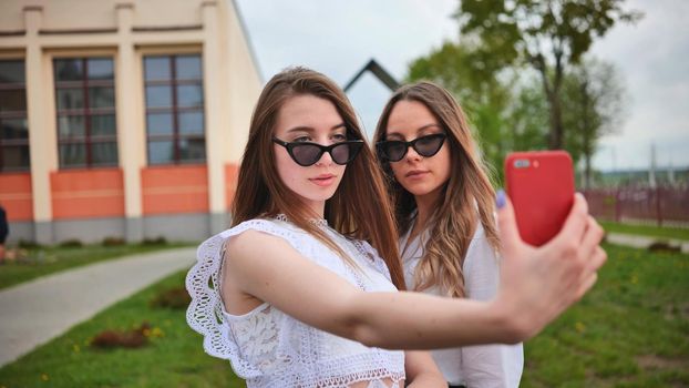 Two girls schoolgirls make a selfie using a smartphone against the background of the school