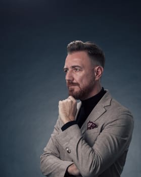 Portrait of a stylish elegant senior businessman with a beard and casual business clothes in photo studio isolated on dark background gesturing with hands. High quality photo