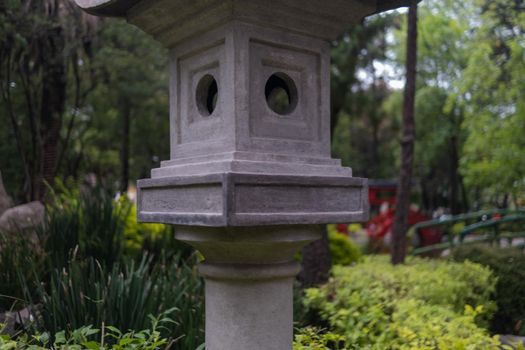 Traditional Japanese stone sculpture surrounded by trees and plants in Masayoshi Ohira Park. Authentic Asian stone bird feeder with vegetation as background. Classic architecture and outdoors