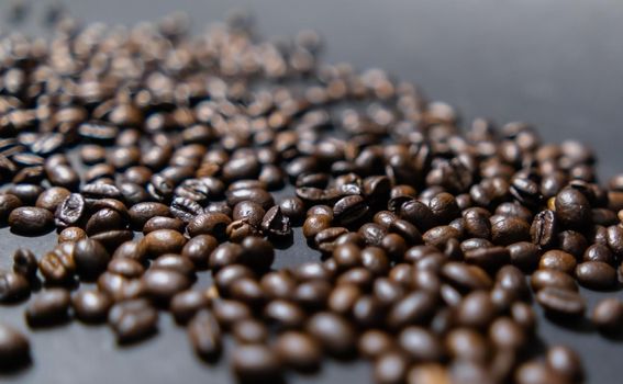 Close-up of small pile of roasted coffee beans with dark gray background. Group of coffee grains scattered on dark color surface. Caffeine and drink preparation