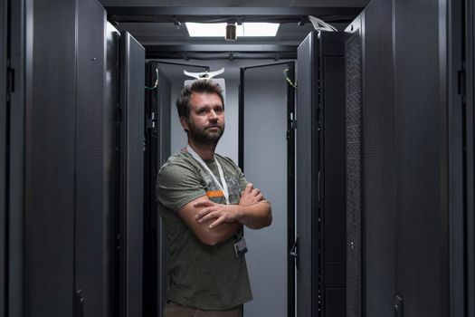 Portrait of male technician or network administrator standing brave as a hero with arms crossed in data center server room. High quality photo