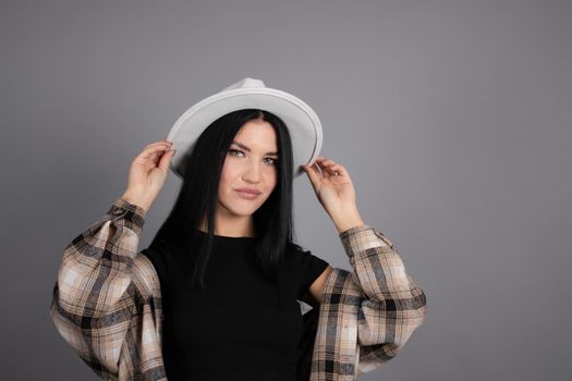 attractive young woman in plaid shirt, white hat and jeans on gray background. pretty female portrait