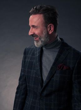 Portrait of a stylish elegant senior businessman with a beard and casual business clothes in photo studio isolated on dark background gesturing with hands. High quality photo