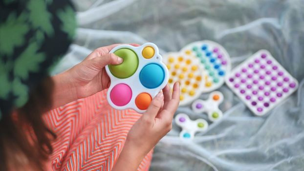 Teen girl plays with anti-stress multicolored toys popit and simple dimple in the park on a summer day