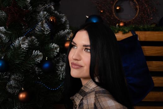 confident beautiful young woman in plaid shirt near christmas tree. new year, winter theme.