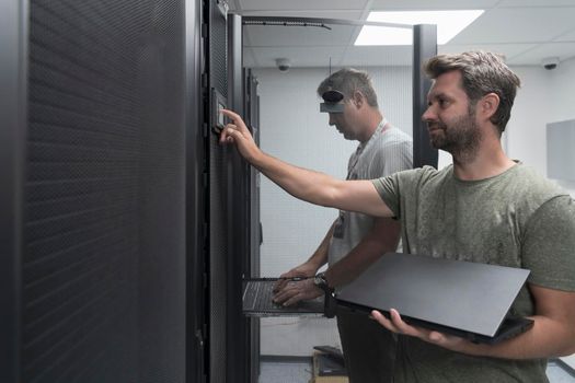 A couple of server engineers cooperate in high tech data centers. Technicians team updating hardware inspecting system performance in super computer server room or cryptocurrency mining farm.