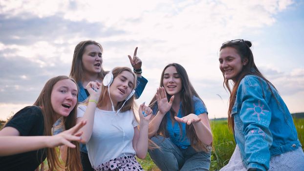 A group of girls of friends are listening to music on headphones and dancing to a friend