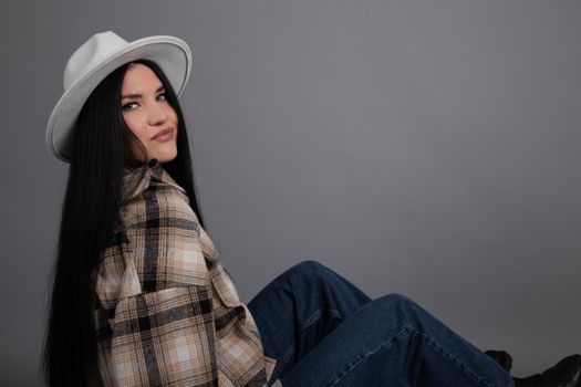 attractive young woman in plaid shirt, white hat and jeans on gray background. pretty female portrait