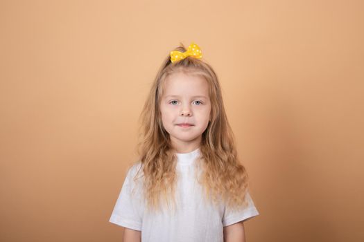 adorable blonde little girl in white t-shirt. on brown - yellow background. innocence child portrait.