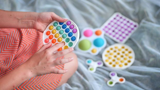 Teen girl plays with anti-stress multicolored toys popit and simple dimple in the park on a summer day