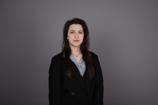 attractive confident brunette business woman in blue blouse and black jacket on grey background.