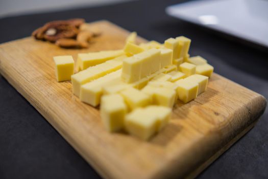 Close-up of diced yellow cheese and walnuts on cutting board. Wooden board with fresh cheese cubes and nuts above black surface. Healthy snacks and balanced diet