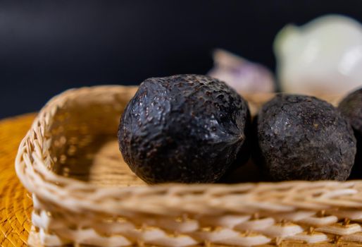 Close-up of three avocados in traditional wooden and palm basket with blurry onion and garlic as background. Fresh black vegetables in handmade basket. Authentic healthy food preparation