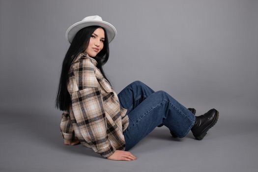 attractive young woman in plaid shirt, white hat and jeans on gray background. pretty female portrait