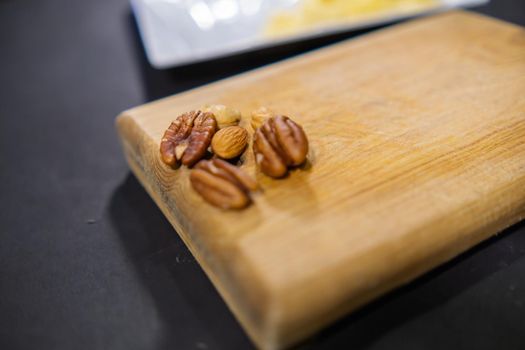 Close-up of a few walnuts, almonds, and Indian nuts on cutting board above black surface. Fresh natural nuts wooden board with blurry background. Tasty traditional snacks