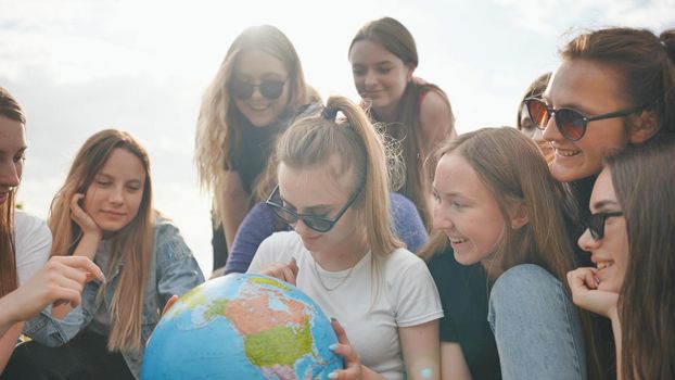 A group of cheerful girls is exploring the globe of the world in the meadow