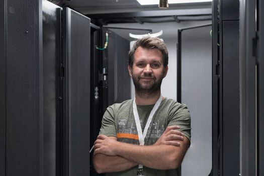 Portrait of male technician or network administrator standing brave as a hero with arms crossed in data center server room. High quality photo