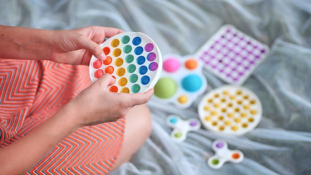 Teen girl plays with anti-stress multicolored toys popit and simple dimple in the park on a summer day