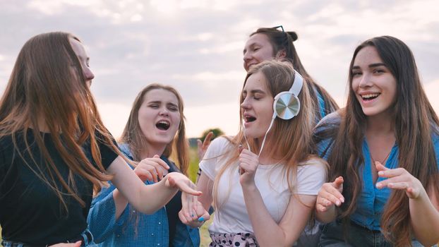 A group of girls of friends are listening to music on headphones and dancing to a friend