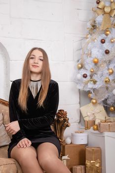 attractive woman in black dress sitting on a golden classic couch near white christmas tree. happy new year.