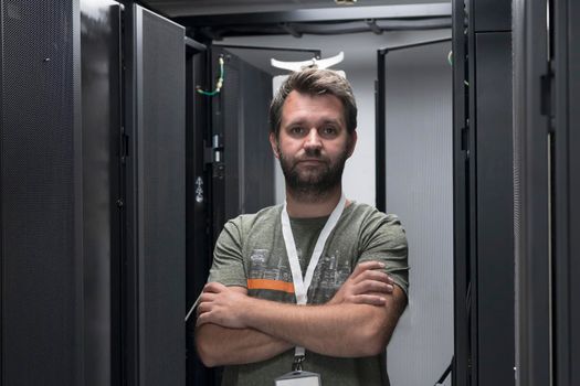 Portrait of male technician or network administrator standing brave as a hero with arms crossed in data center server room. High quality photo