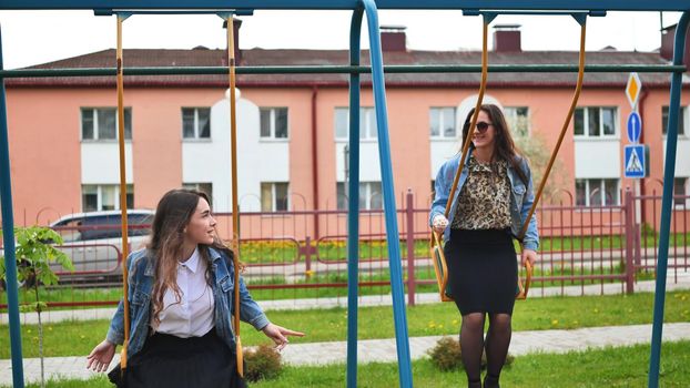 Joyful schoolgirls ride a swing in summer day