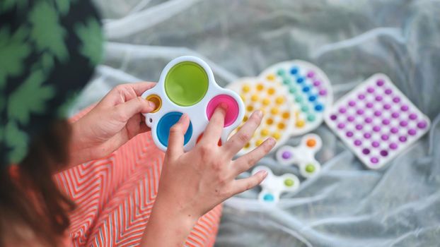 Teen girl plays with anti-stress multicolored toys popit and simple dimple in the park on a summer day