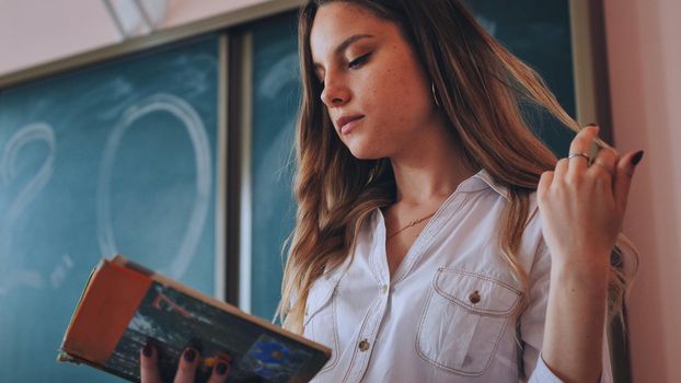 Cute schoolgirl reads a book in class