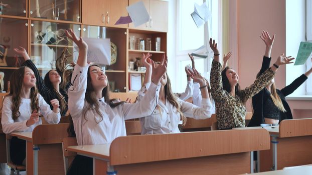 Pupils sitting at their desks in the classroom throw notebooks up. Group of students to complete academic year.