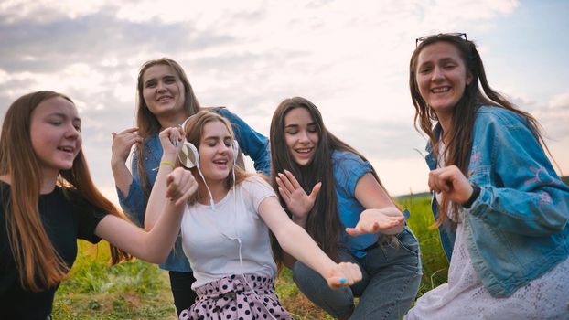 A group of girls of friends are listening to music on headphones and dancing to a friend