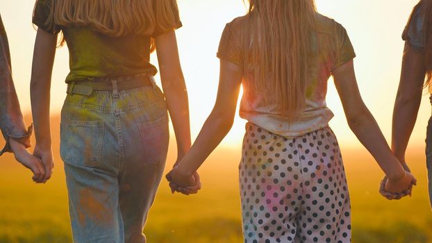 Eleven cheerful girls run to the meeting across the field in the summer, holding hands