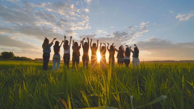 Silhouette of friends of 11 girls waving their hands at sunset in the field