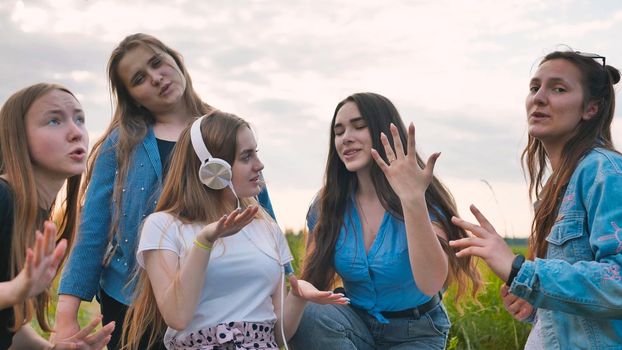 A group of girls of friends are listening to music on headphones and dancing to a friend