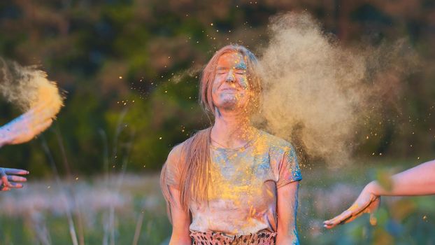 Friends sprinkle their cheerful girlfriend with multi-colored powder. Holi holiday