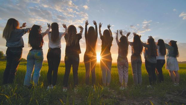 Silhouette of friends of 11 girls waving their hands at sunset in the field