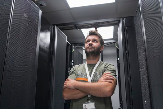 Portrait of male technician or network administrator standing brave as a hero with arms crossed in data center server room. High quality photo