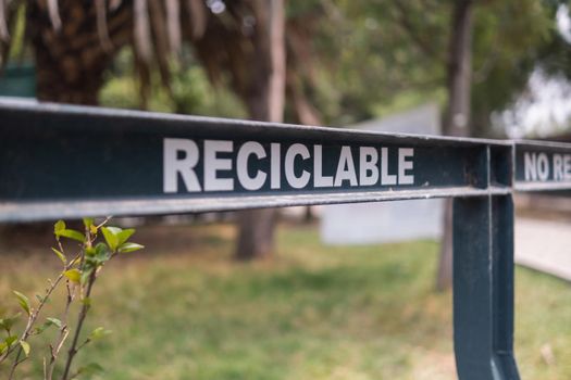 Close-up of Spanish sign for recyclable trash in park from Mexico City. White capital letters in black metal bar with blurry trees as background. Environment and outdoors