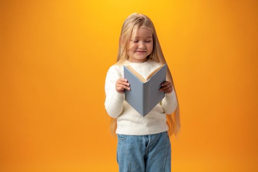 Little beautiful smiling girl holding book against yellow background, close up