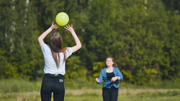 Two girlfriends play volleyball in the meadow