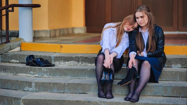Tired schoolgirls sit barefoot on the steps of the school