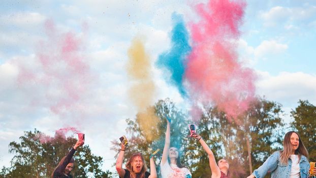 Cheerful girls toss up multi-colored powder at a beautiful sunset