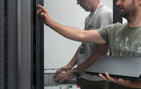 A couple of server engineers cooperate in high tech data centers. Technicians team updating hardware inspecting system performance in super computer server room or cryptocurrency mining farm.