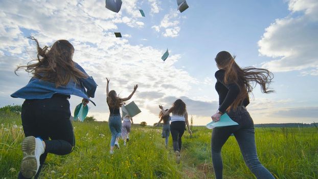 Cheerful students run throwing notebooks after school at sunset