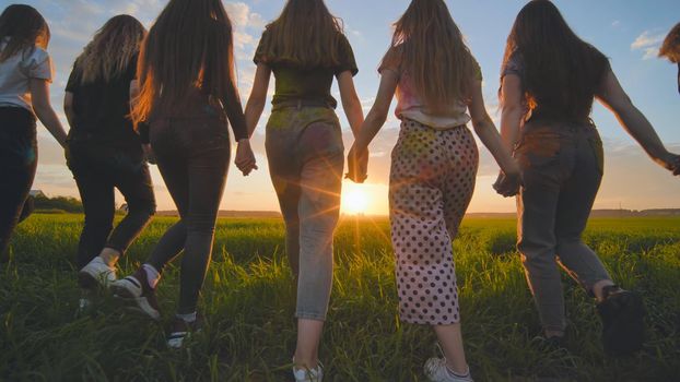 A group of girls walk towards the sun at sunset holding hands