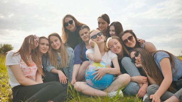 A group of cheerful girls is exploring the globe of the world in the meadow