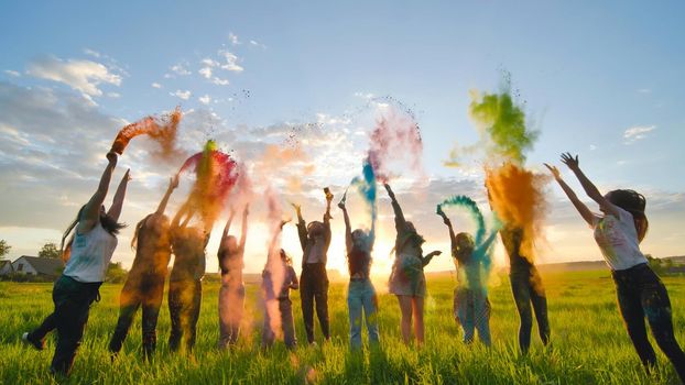 Cheerful girls toss up multi-colored powder at a beautiful sunset