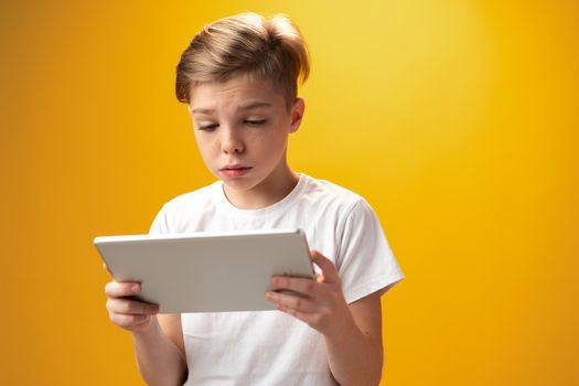 Little boy playing with digital tablet against yellow background, close up