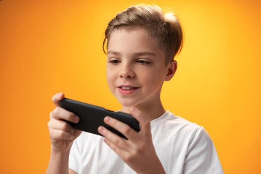 Little kid playing games on smartphone over yellow background, close up