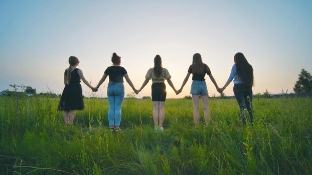 Girls friends go hand in hand at sunset across the field